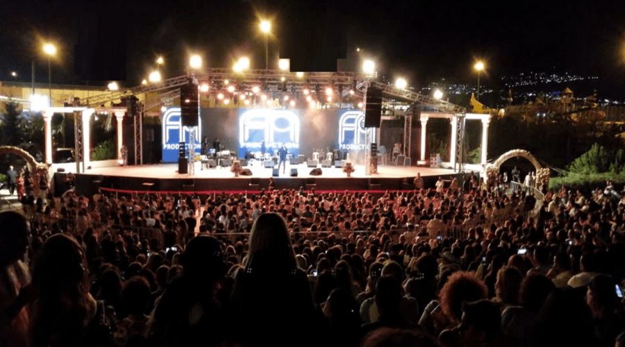 The lit stage and full amphitheatre seen from the back of the crowd